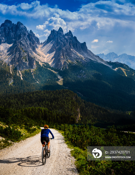 Tourist cycling in Cortina dAmpezzo, stunning rocky mountains on the background. Woman riding MTB e