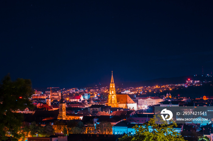 Landscape of city buildings at night with intense colorful lights and a clock tower in the middle – 