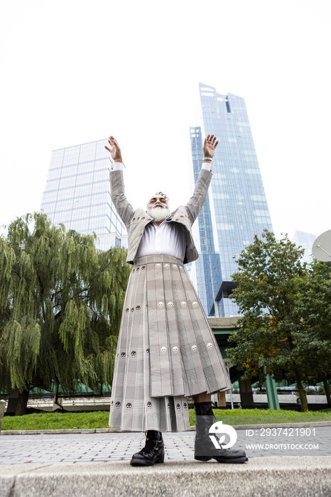 man with gray hair and beard wearing skirt suit with city view, arms raised