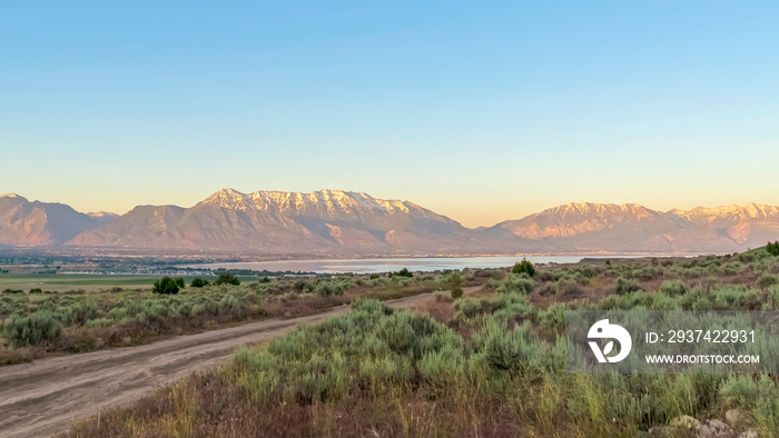 Panorama Rough road on grassy terrain with view of scenic lake and snow capped mountain