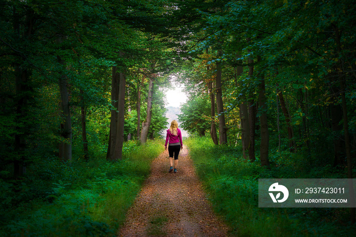 Blonde woman walking on a straight path to a forest clearing in a mystical forest