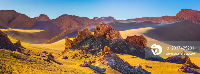 Desert landscape in the Atacama desert with bare rocks and sand dunes in warm late afternoon light