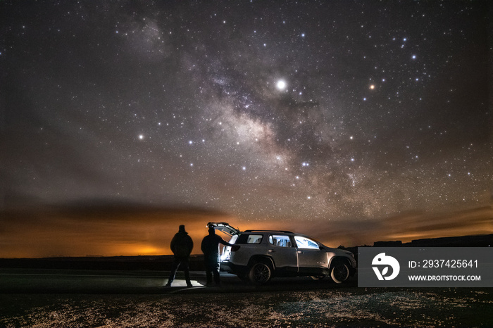 Two silhouettes of people standing under  the Milky Way stretching across the night sky. Adventure s