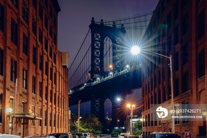 Brooklyn bridge seen from a narrow alley enclosed by two brick buildings at dusk, NYC USA