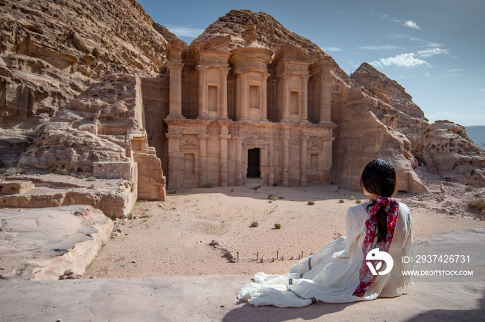 Asian woman tourist in white dress sitting at Ad Deir or El Deir, the monument carved out of rock in