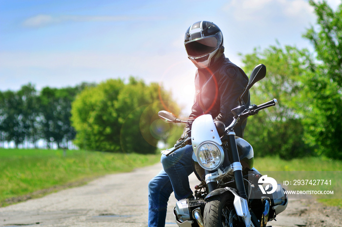 戴着头盔和皮夹克的摩托车手坐在户外的摩托车上。摩托车回来了