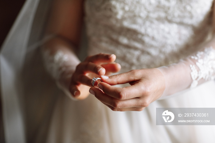 cropped photo of gentle hands of the bride standing in a white lace dress puts a wedding ring on her