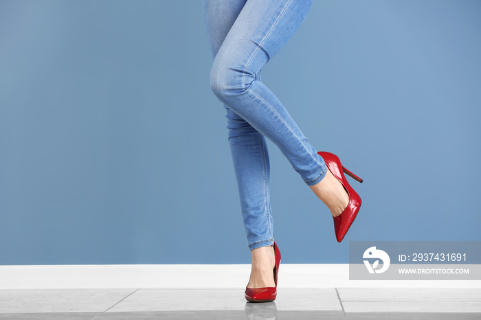 Young woman in high-heeled shoes against color wall