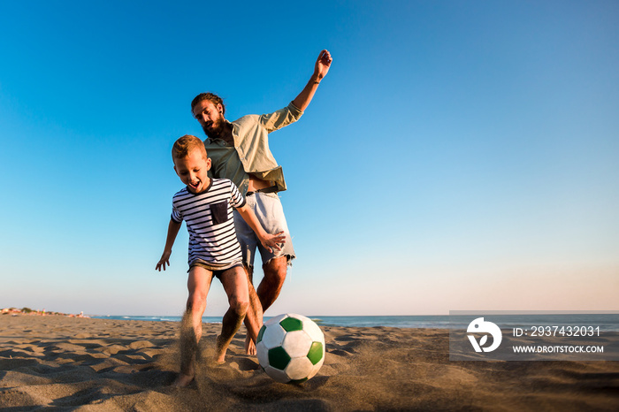 Happy father and son play soccer or football on the beach having great family time on summer holiday