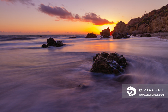 Waves wash over a rock as the sun sets in Malibu