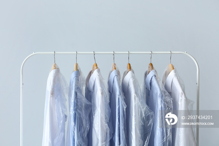 Rack with clean shirts in plastic bags on grey background