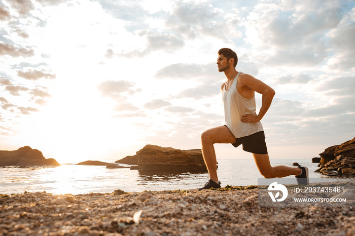 Young healthy man athlete doing squats at the beach