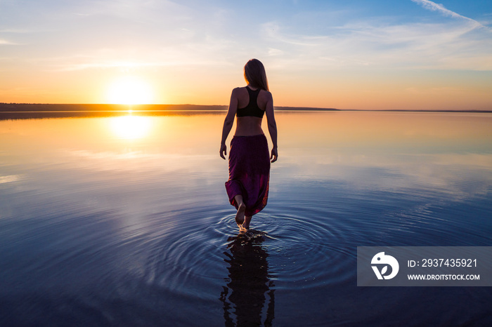 Silhouette woman on the beach at sunset . She stands in water. Morning natural stretch warm-up train