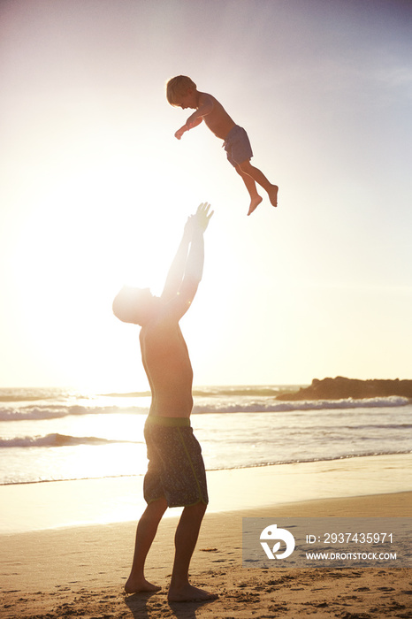 父亲站在晴朗的天空下的海滩上，把儿子抛向空中