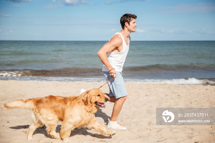 英俊的年轻人带着狗在海滩上奔跑