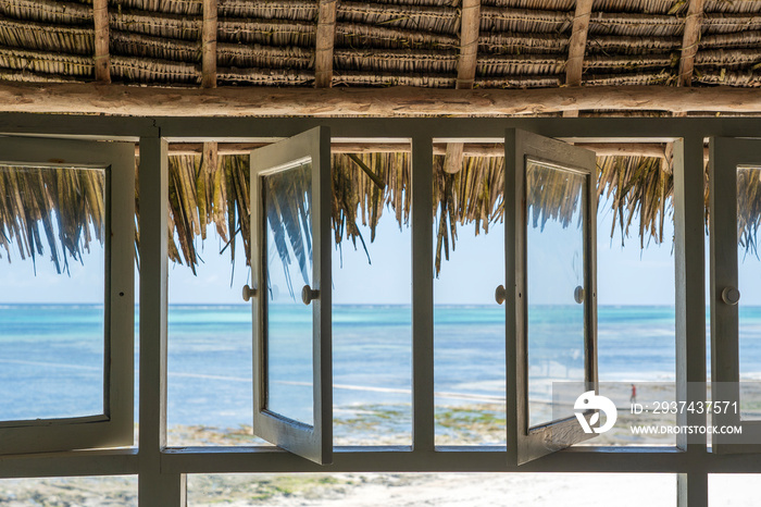 Open windows of thatched roof veranda overlooking the turquoise ocean on the island of Zanzibar, Tan