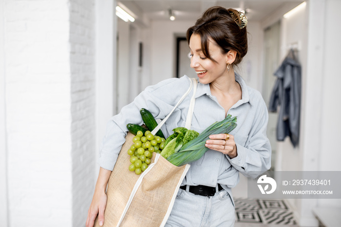 Portrait of a young and cheerful woman standing with shopping bag full of fresh vegetables and green