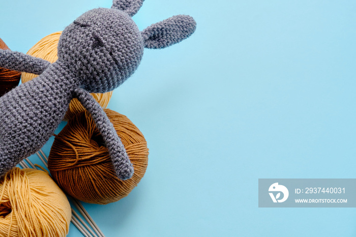 Top view of the bright color yarn clews with grey stuffed amigurumi bunny on the blue background. Co