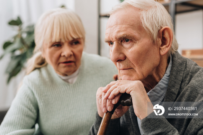 selective focus of sad pensioner sitting near senior wife at home