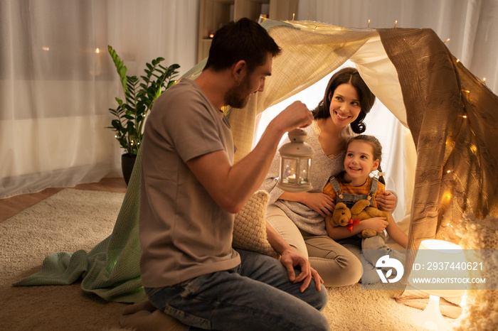 family, hygge and people concept - happy mother, father with lantern and little daughter with teddy 