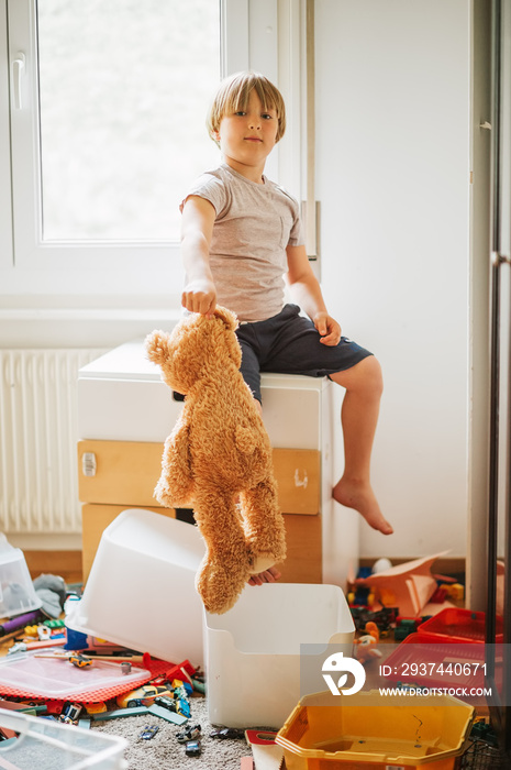 Indoor portrait of a child playing in a very messy room, throwing teddy bear on the floor