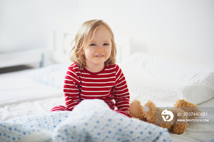 Happy toddler girl in striped red and white pajamas sitting on bed