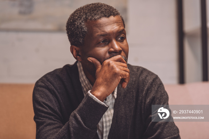 depressed african american man looking away while holding hand near face