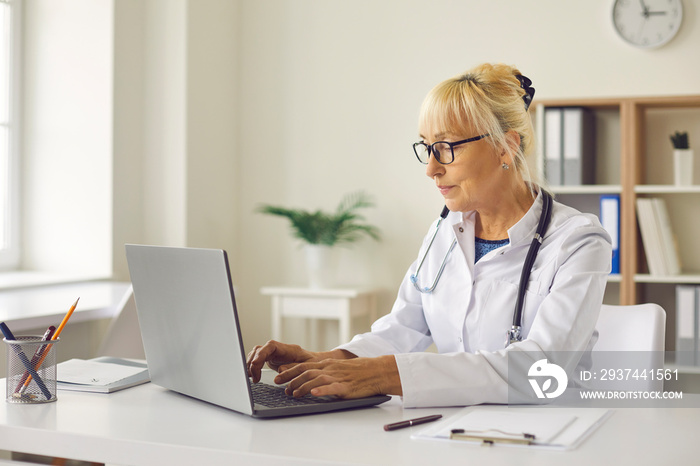 专注的资深女医生坐在办公室的笔记本电脑前，进入患者诊断