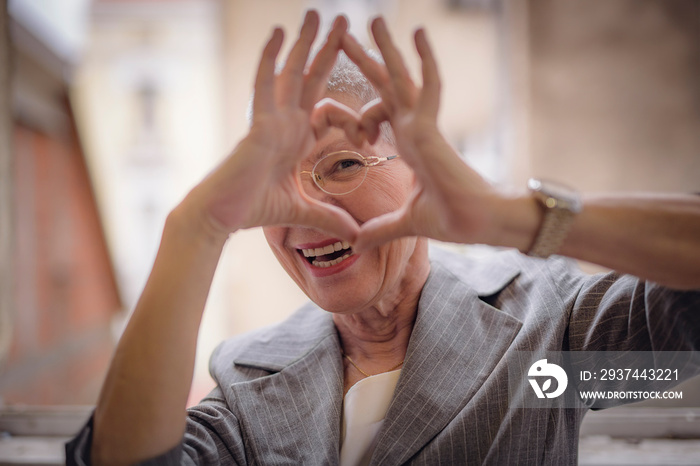 Cute senior old business woman making a heart shape with her hands and fingers