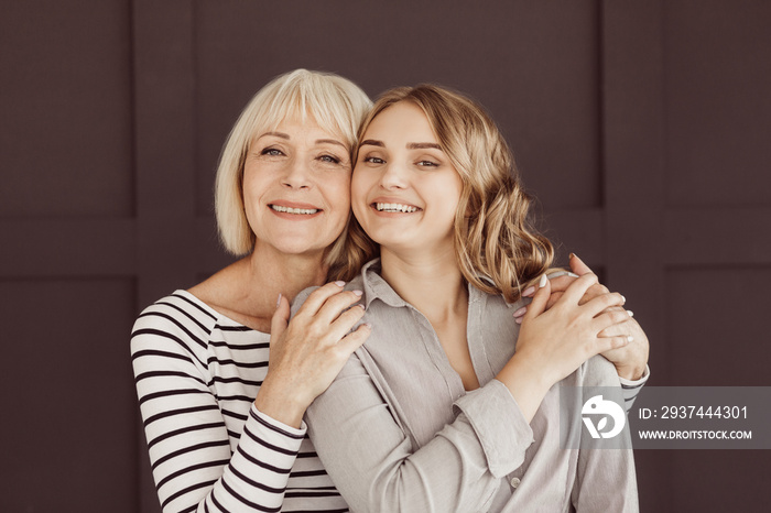 Senior woman and young daughter hugging against brown wall