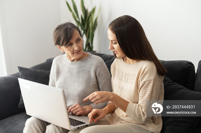 An adult daughter is teaching to senior mother how to pay bill online, web searching, explains to ma