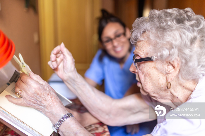 快乐的老年妇女和她的看护人在家看书。老年家庭护理概念。