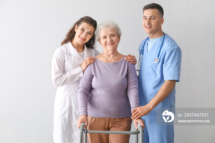 Young medical workers with senior woman on grey background