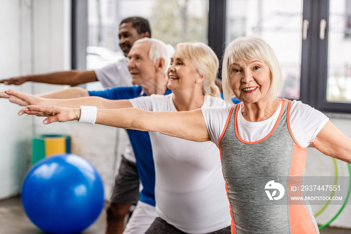 happy senior multiethnic sportspeople synchronous exercising at sports hall