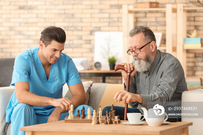 Young caregiver and senior man playing chess at home