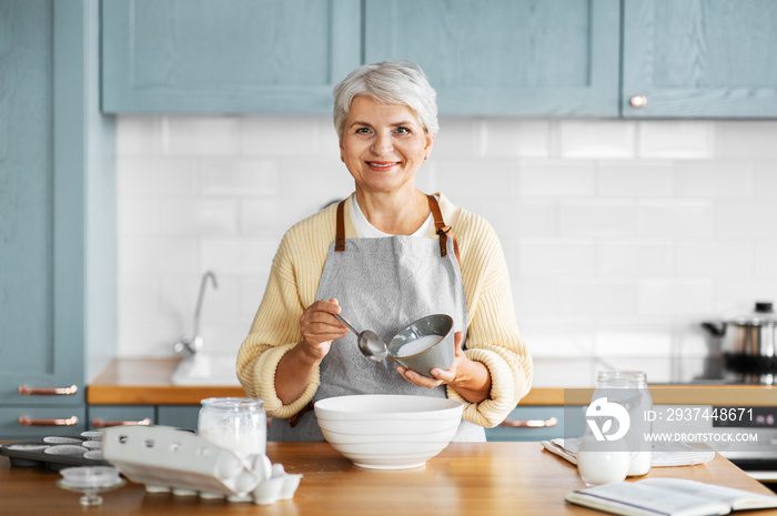 people and culinary concept - happy smiling woman cooking food on kitchen at home and adding sugar