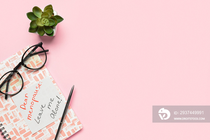 Notebook with text DEAR MENOPAUSE LEAVE ME ALONE, pen, eyeglasses and flowerpot on pink background