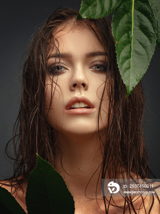 Beauty portrait of a young beautiful girl with wet hair and green leaves.
