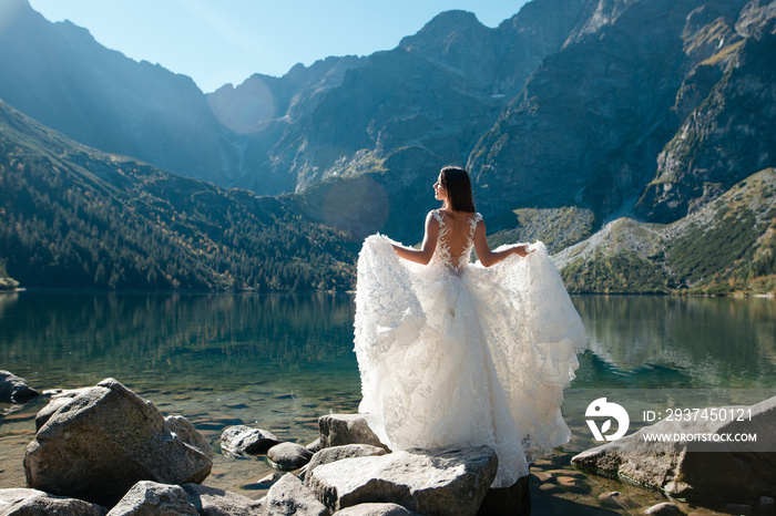 Back view of bride in beautiful wedding dress standing on the lake shore with scenic mountain view