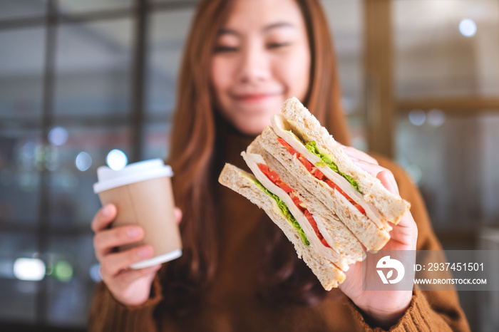 Closeup image of an asian woman holding whole wheat sandwich and coffee cup