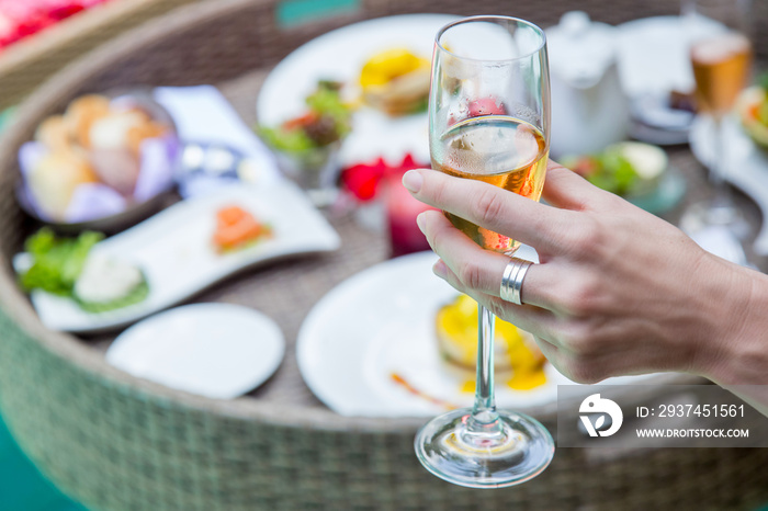 Close up image of a woman holding a glass of champagne, a meal next to the pool, leisure vacation tr