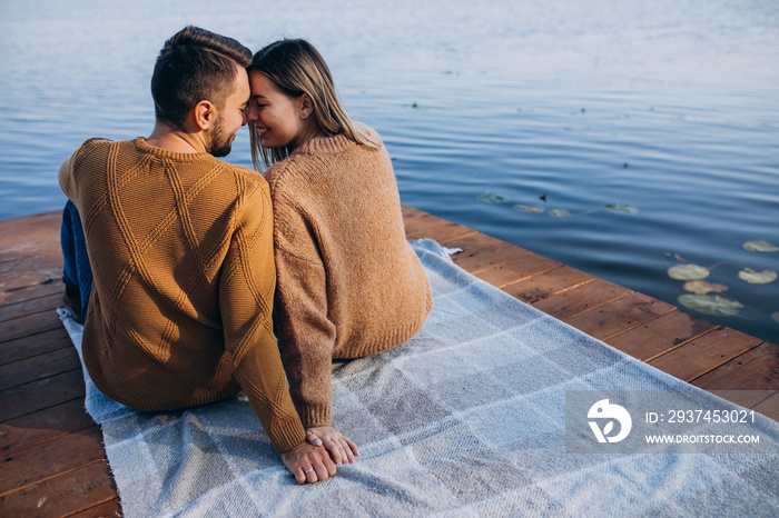 年轻夫妇坐在河边的甲板桥上，欣赏湖景