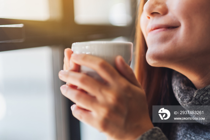 Closeup image of a beautiful asian woman holding and smelling a cup of hot coffee