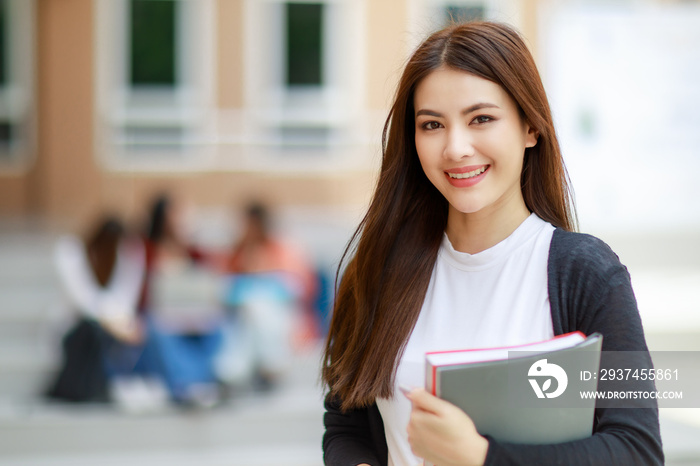 年轻漂亮的亚洲大学生女孩拿着书，和一群朋友合影