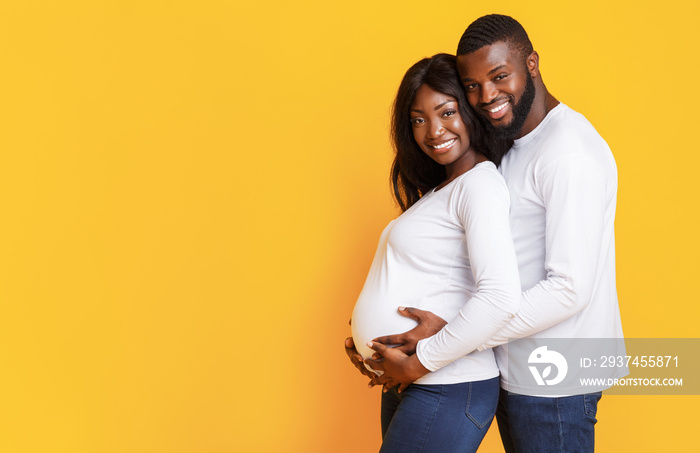 Pregnant afro woman and her husband embracing over yellow background