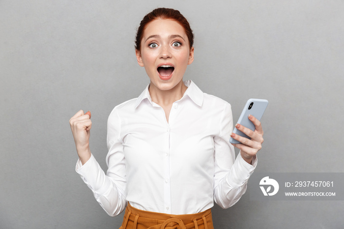 Redhead business woman posing isolated over grey wall background using mobile phone.