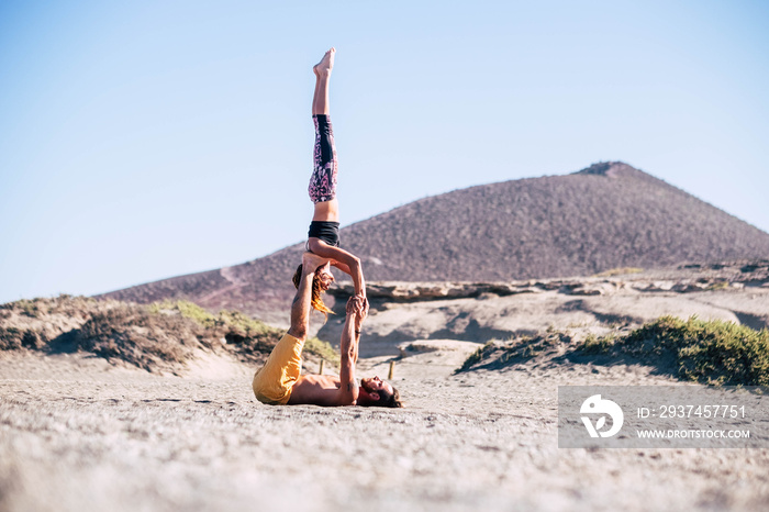 couple of two adults doing acroyoga together at the beach on the sand - man holding his teammate wit