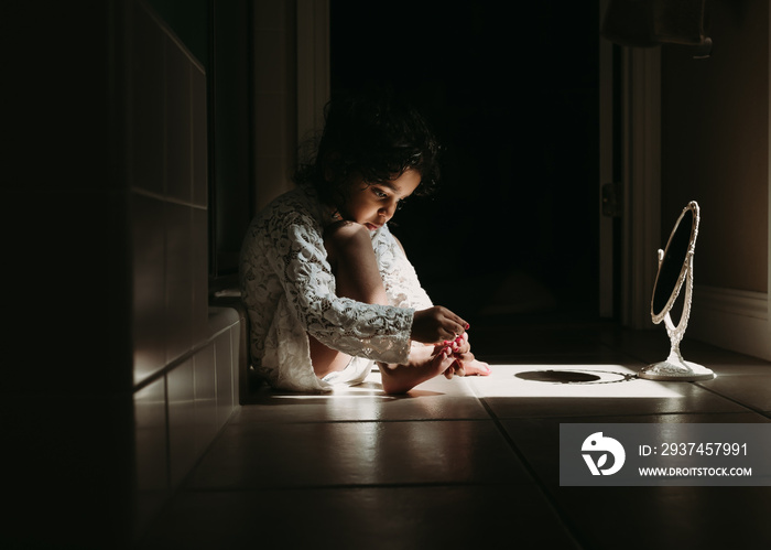 A little girl putting nail polish on her toes in beautiful light 