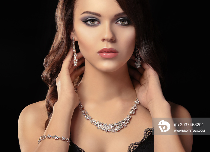 Portrait of beautiful young woman with luxury jewelry on dark background