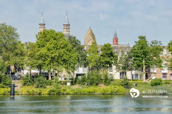 Green trees on the banks of the Maas river, a street, houses, the towers of the basilica of Our Lady